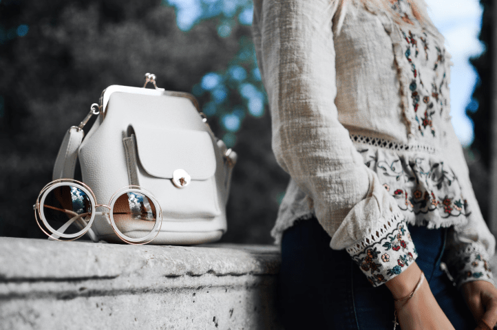 Torso of a person sitting next to a bag and a pair of glasses