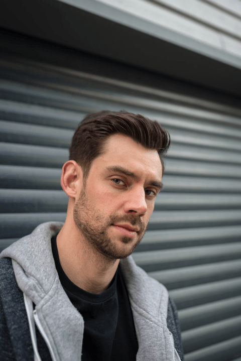 An upper body photo of a person looking at the camera standing in front of a garage door.
